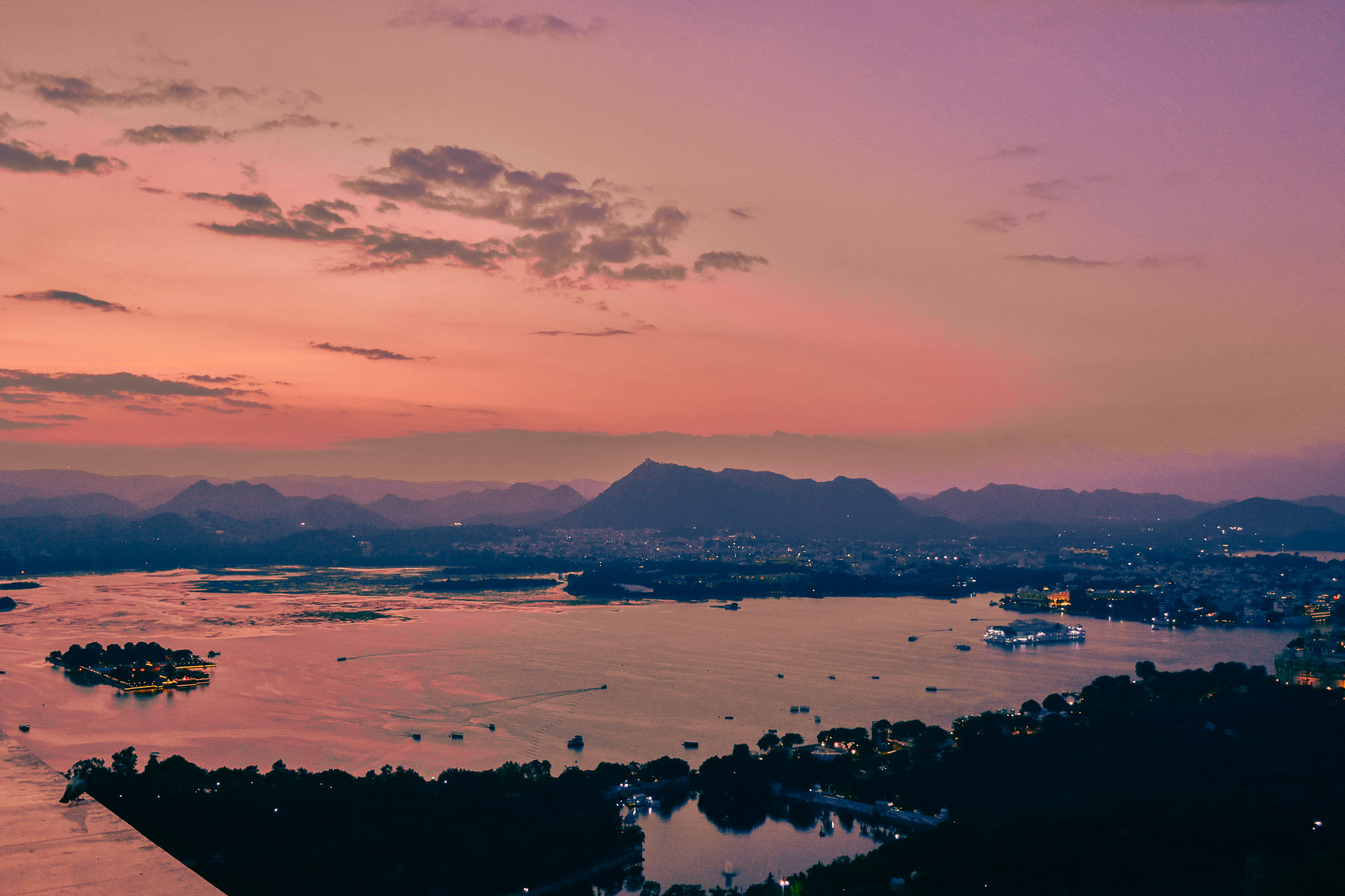 Orange sunset gradient over Udaipur with warm evening light across the lake.